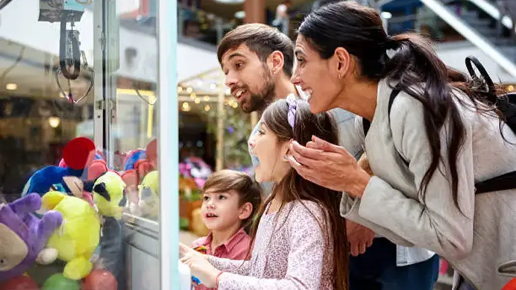 little girl playing claw machine with family in fecs