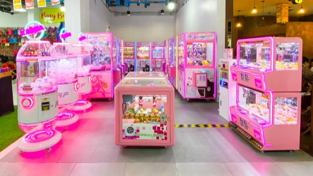 Row of glowing pink claw machines filled with prizes at an indoor arcade market.