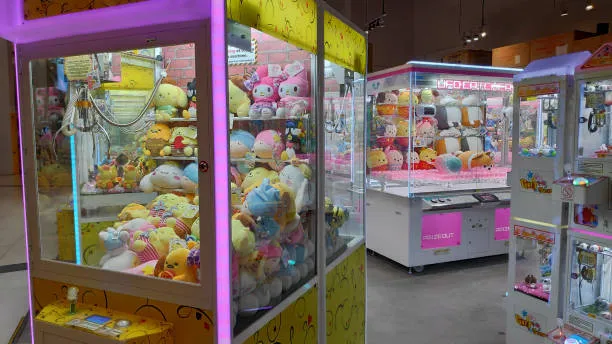 A row of brightly lit claw crane vending machines filled with colorful stuffed animals and plush toys.